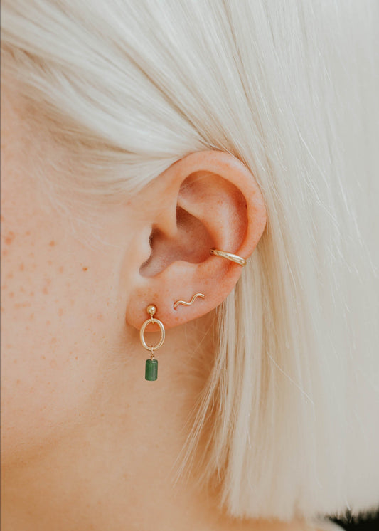 Close-up of an ear wearing gold hoop earrings with a green gemstone.