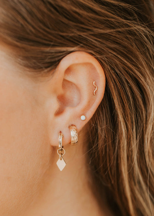 Close-up of an ear with gold earrings and an opal, with blurred hair in the background