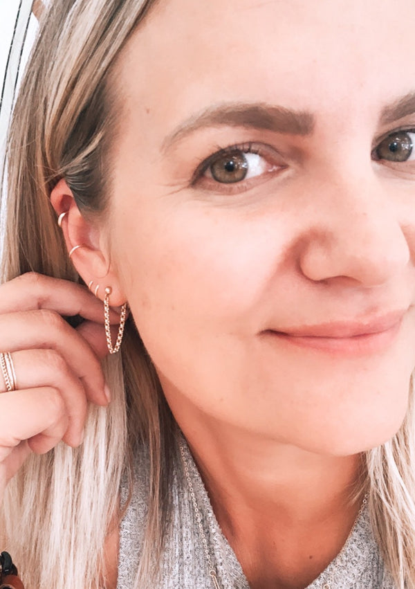 Hello Adorn's owner Jess showing off her earring stack using a twist earring, a gold chain earring in Annex Stud style, and two ear cuffs in the Ear Cuff Duo style for people with no piercings and styled with a simple ring stack.