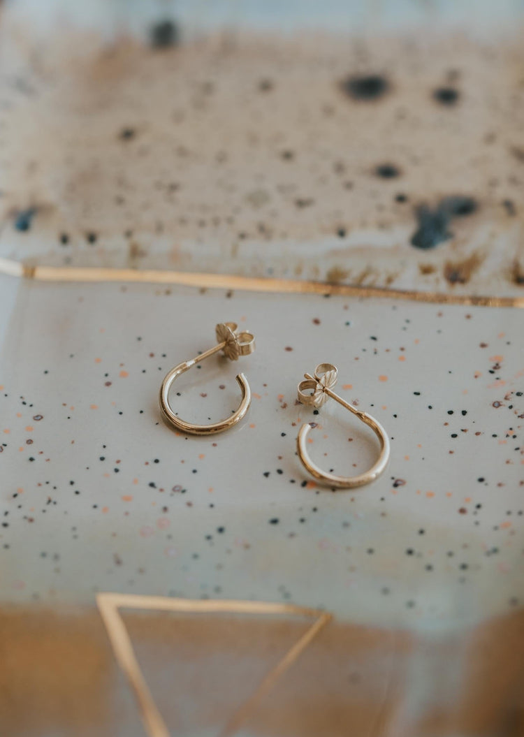 Small gold earrings in everyday hoops style by Hello Adorn shown with an earring back.