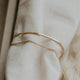 A close up look at a gold cuff bracelet in the Tides Cuff style from Hello Adorn, a simple cuff bracelet with a chain bracelet attached, a staple piece for any bracelet stack.