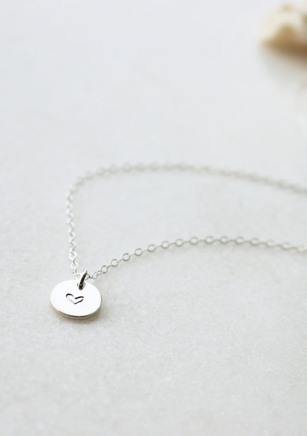 A silver custom necklace pendant created as a heart necklace that includes a symbol stamped on jewelry by Hello Adorn.