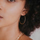 A pair of gold skinny hoops in Cypress Hoops design by Hello Adorn in the largest hoop earring to add to your everyday jewelry collection.