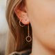 An earring stack in 14k gold fill featuring Hello Adorn's Monday Backdrop which is a dangle earring attached to a stud earring with a circle attached at the end of a chain styled with a hoop earring and a twist earring.