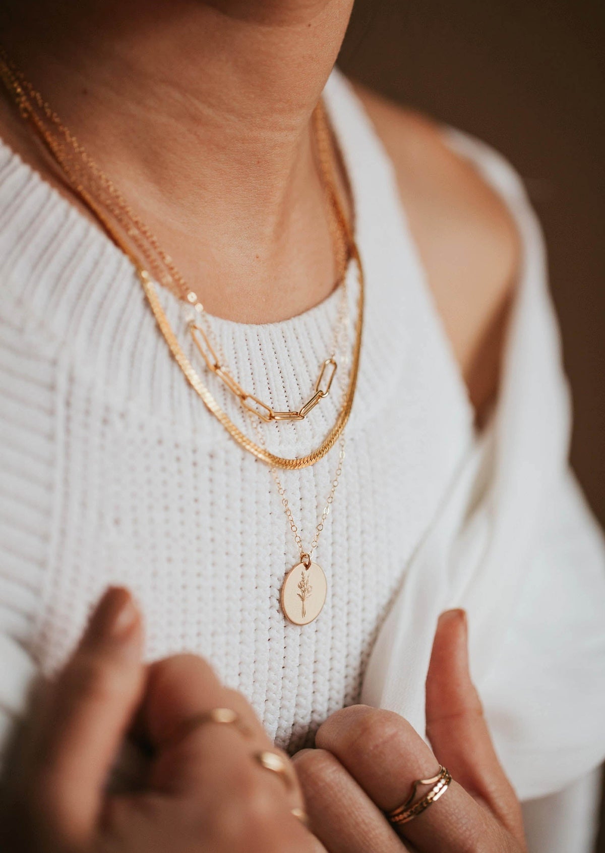 A necklace layering idea featuring a paperclip necklace linked to a dainty chain necklace paired with a necklace with flower and a thick layering chain necklace handmade by Hello Adorn.
