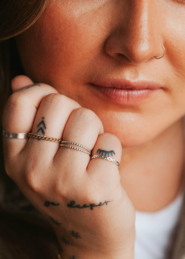 A mixed metal jewelry idea featuring two beaded rings, a braided ring, a chain ring, and a thick ring handmade by Hello Adorn.