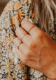 An idea of how to stack rings on fingers to create a gold ring stack using a wave ring in Squiggle Ring design, a thin ring, chain ring, beaded and textured ring, and a hammered ring by Hello Adorn.