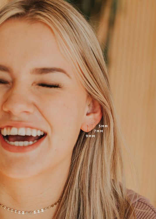 Small gold hoop earring being shown on model in three sizes in 5MM, 7MM, and 9MM styled with confetti chain by Hello Adorn.